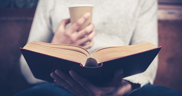 A student sitting with a cup while reading a book