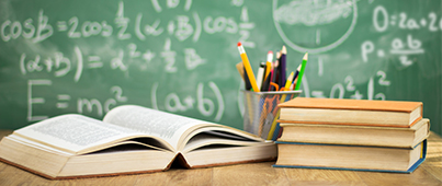 A desk in front of a chalkboard with an open book and a stack of books in front of a pencil case