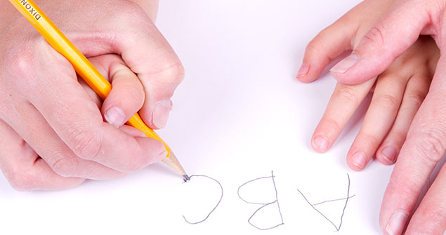 An adult guiding a child's hands while writing