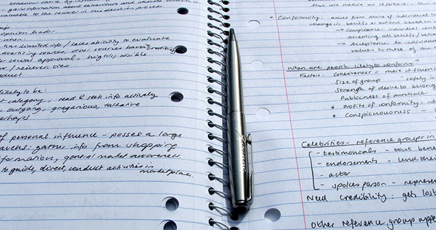 A pen laid down on an open notebook full of notes