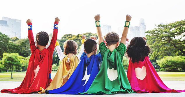 A group of children outdoors dressed up as super heroes raising their arms