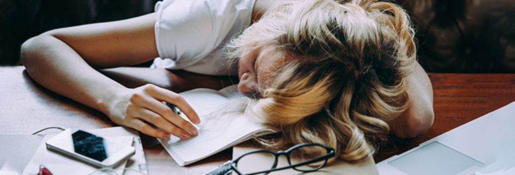 A girl who has fallen asleep on her notebook at her desk while studying