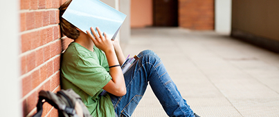 A student sitting up against a wall with their notebook over their head