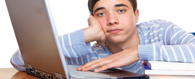 A boy sitting at his laptop looking frustrated